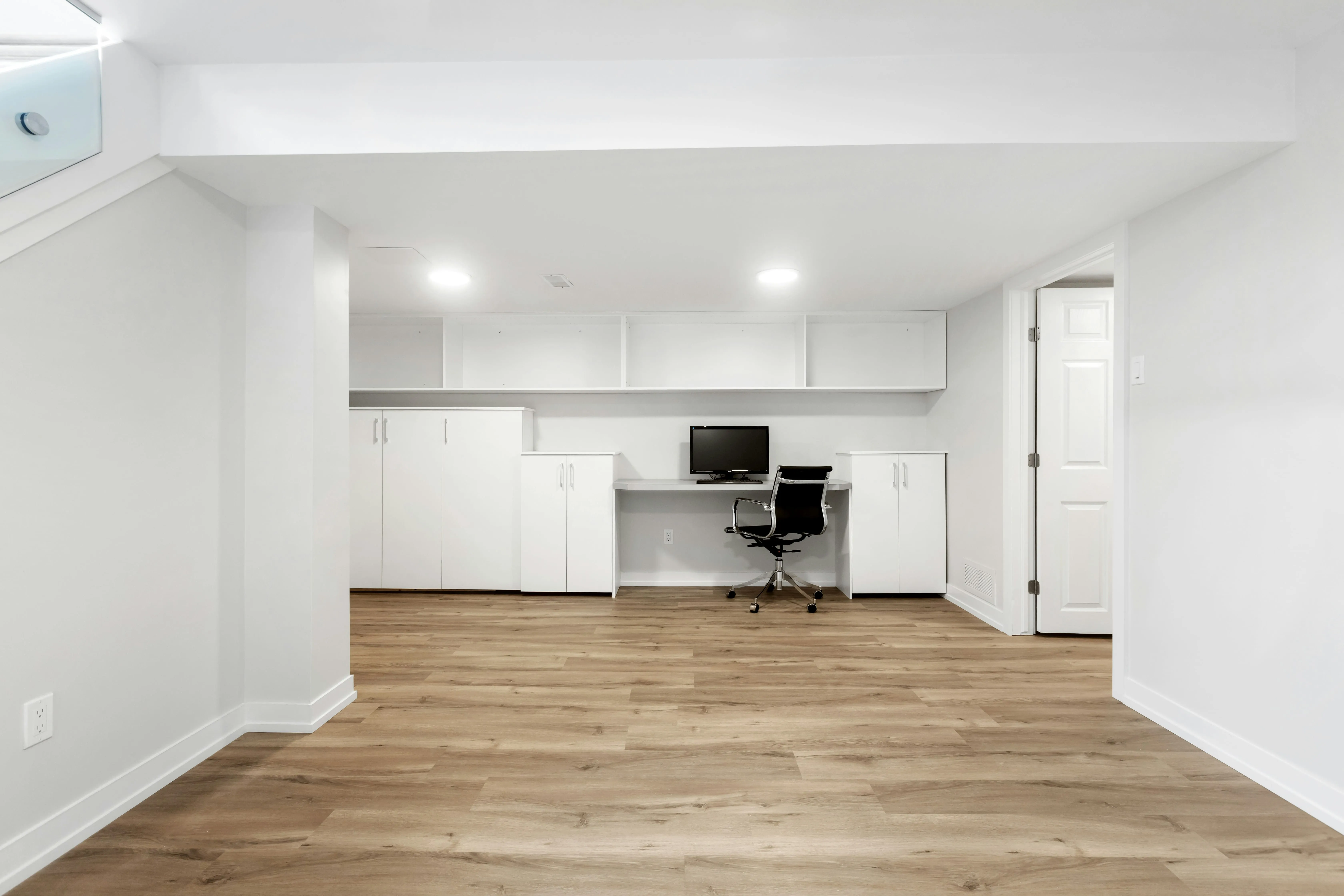 Finished basement work zone with built-in desk, storage cabinets, white walls, and warm flooring
