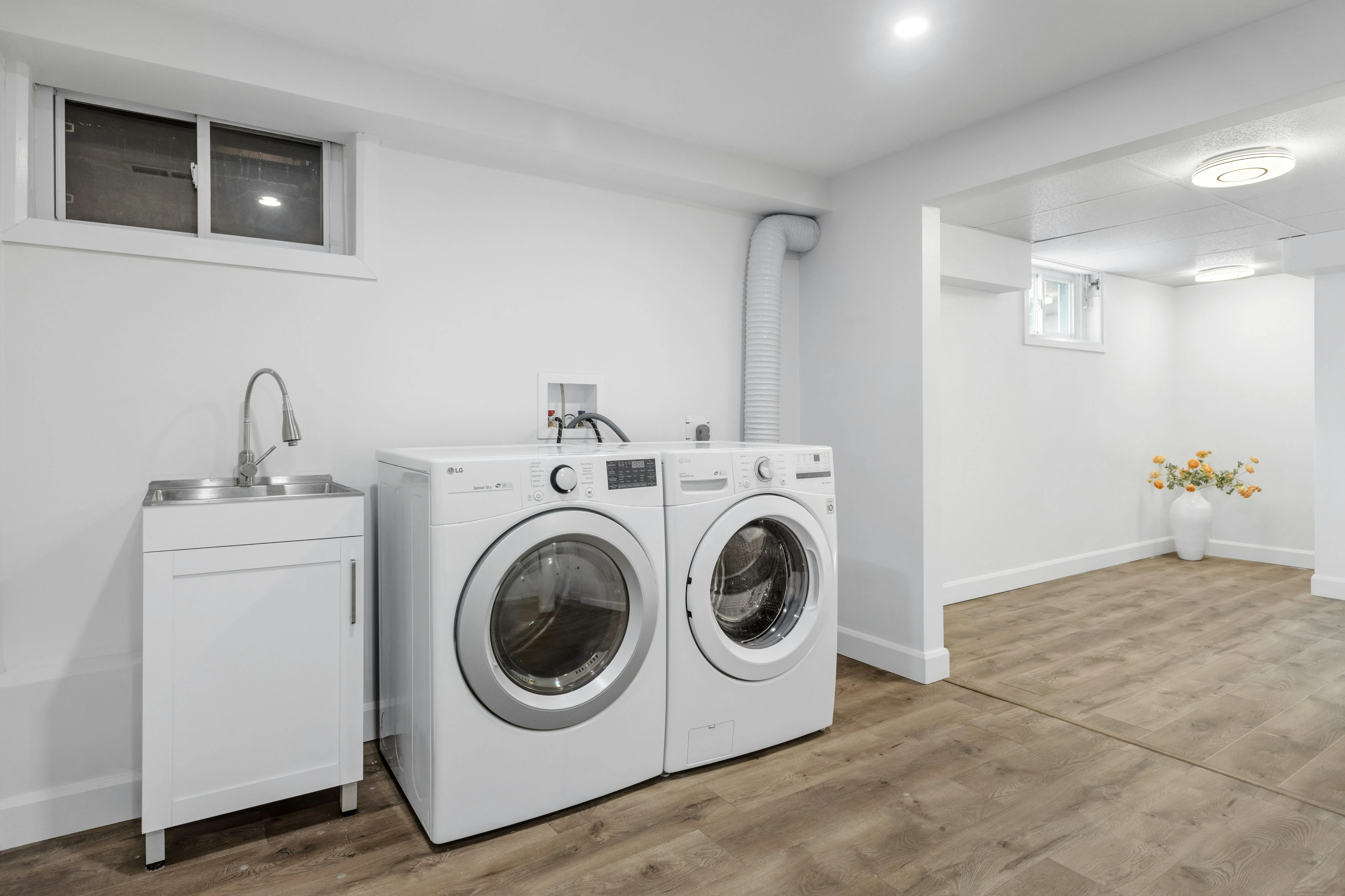 Laundry area with washer, dryer, utility sink, white walls, and warm wood-look flooring