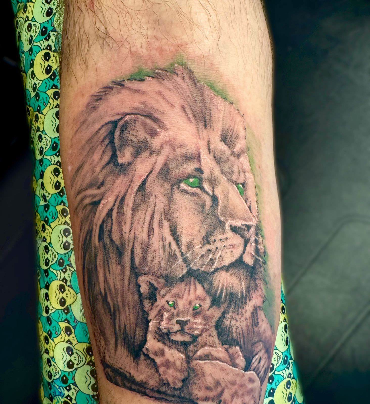 Realistic lion and cub tattoo on the forearm, with a green eye accent