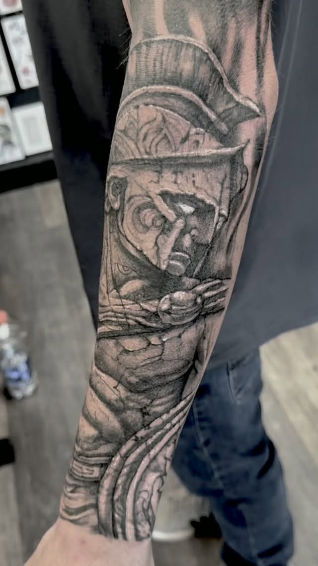 Black-and-grey warrior helmet sleeve tattoo on the forearm