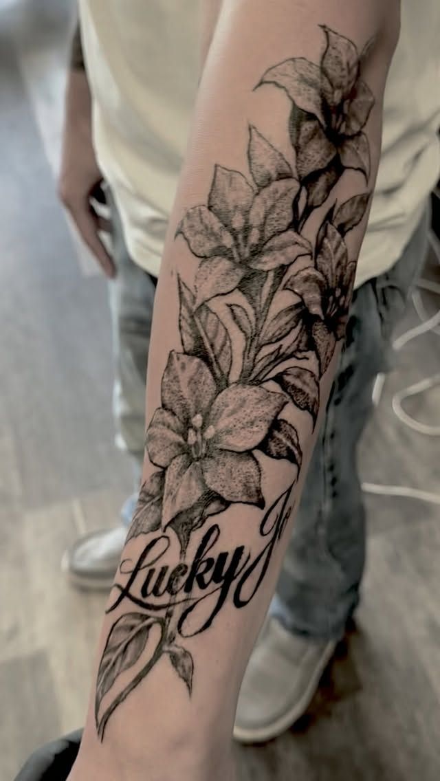 Fine-line floral forearm tattoo with Lucky script lettering