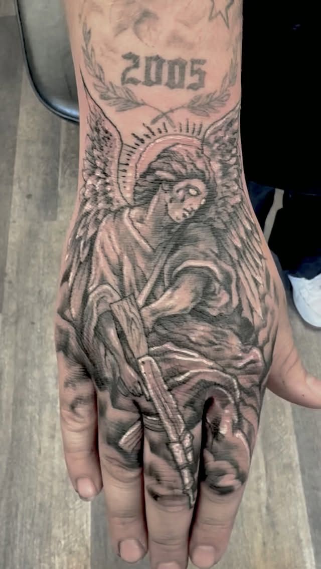 Black-and-grey angel tattoo covering the back of the hand, with 2005 lettering on the wrist