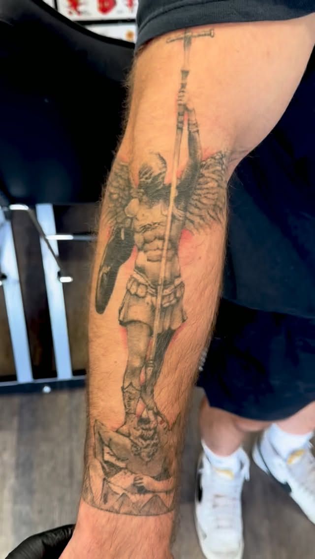 Healed black-and-grey winged warrior tattoo on the forearm, about one year old