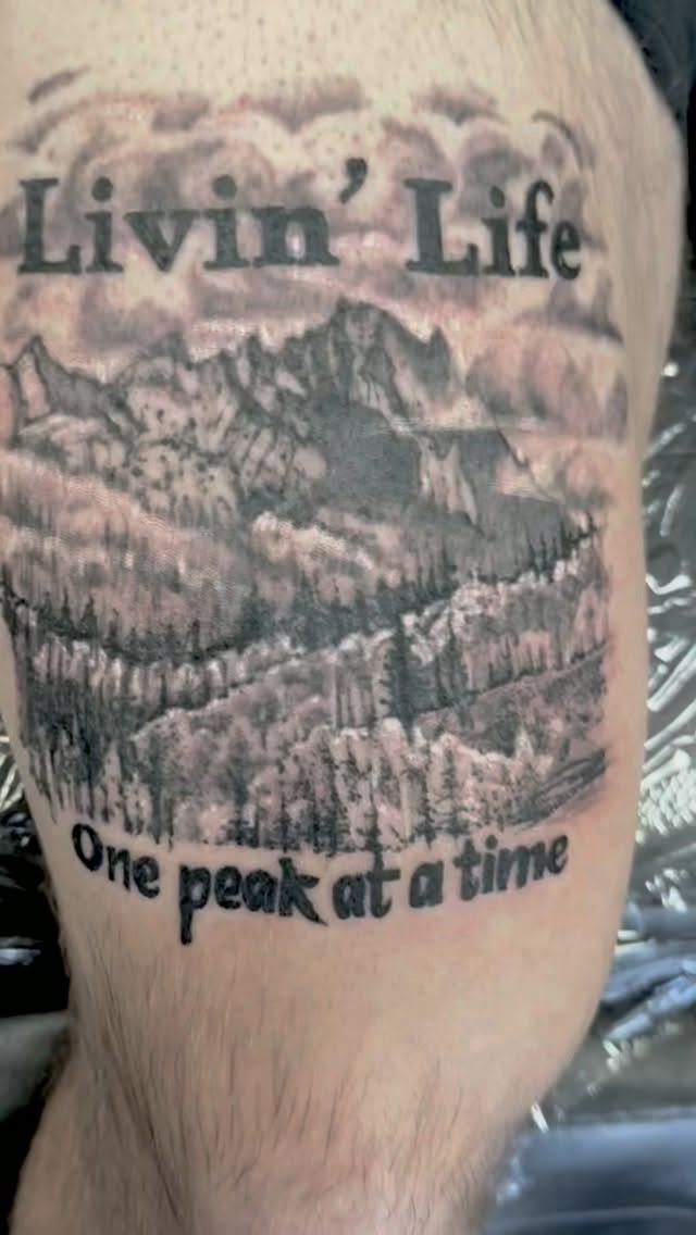 Black-and-grey mountain landscape tattoo with Livin' Life, One peak at a time lettering