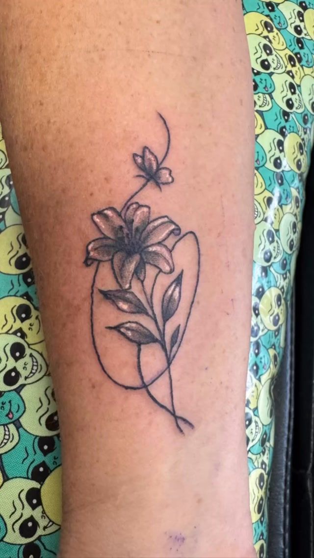 Fine-line lily flower tattoo on the forearm
