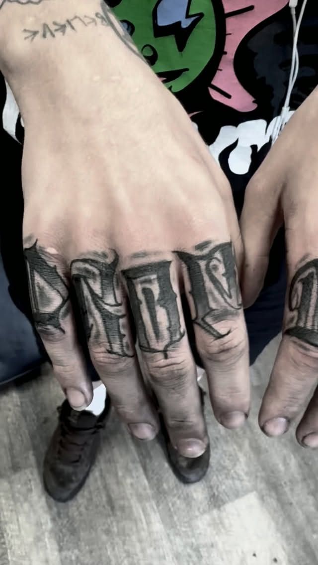 Blackletter knuckle lettering tattoo across the fingers