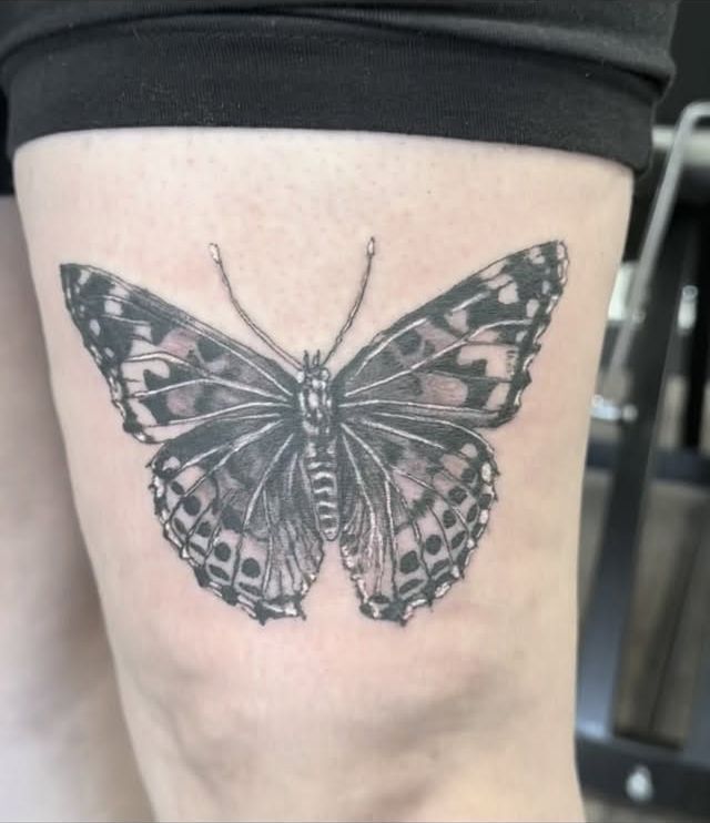 Black-and-grey realistic butterfly tattoo above the knee