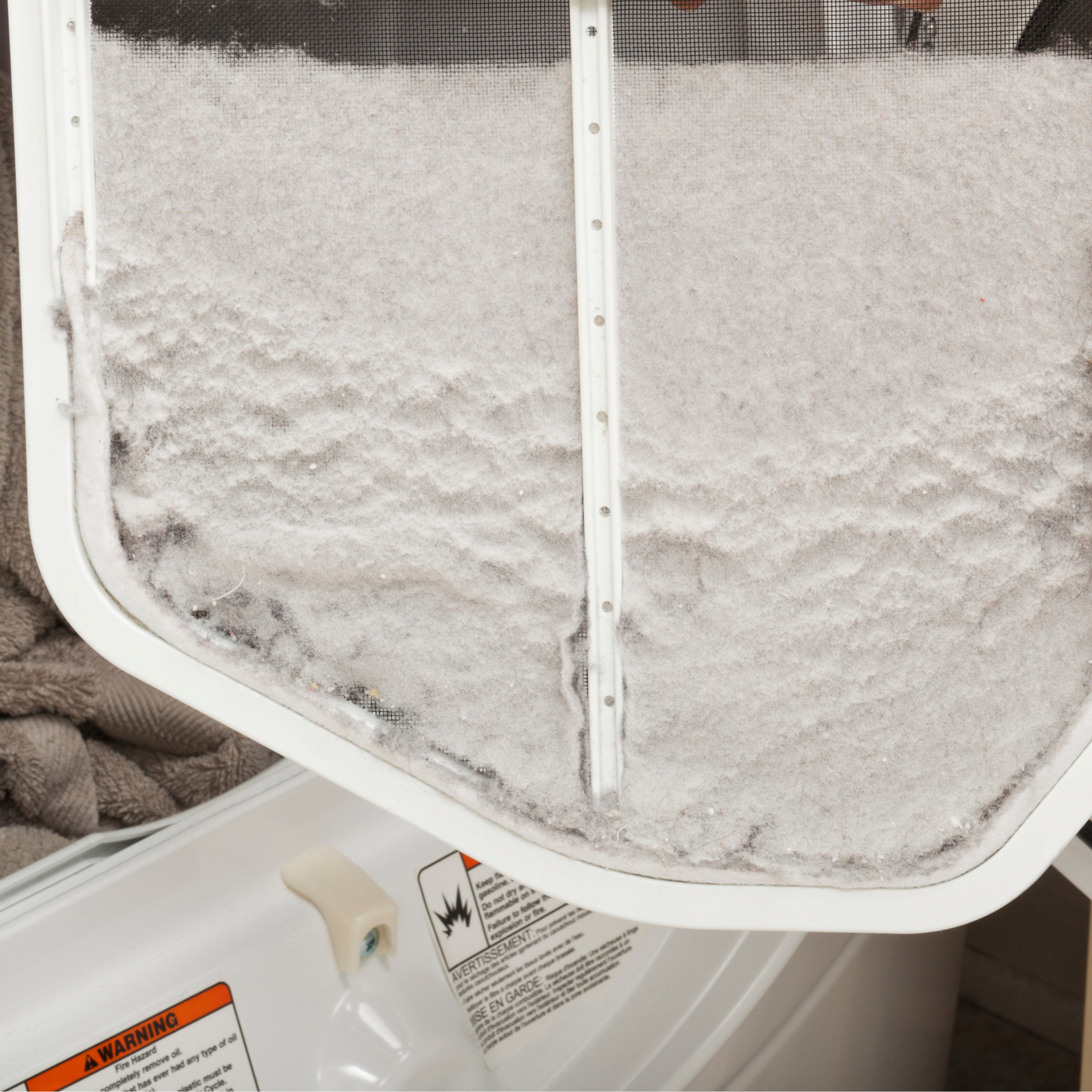 Image is of a dirty dryer vent hose and lint build up behind the dryer. There is also a hanger, dryer sheets and lint on the floor