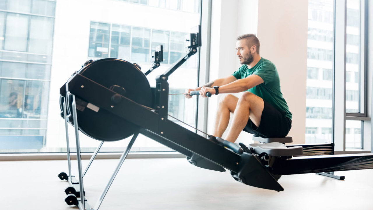 Man doing an indoor rowing machine workout in a bright fitness studio with city views.