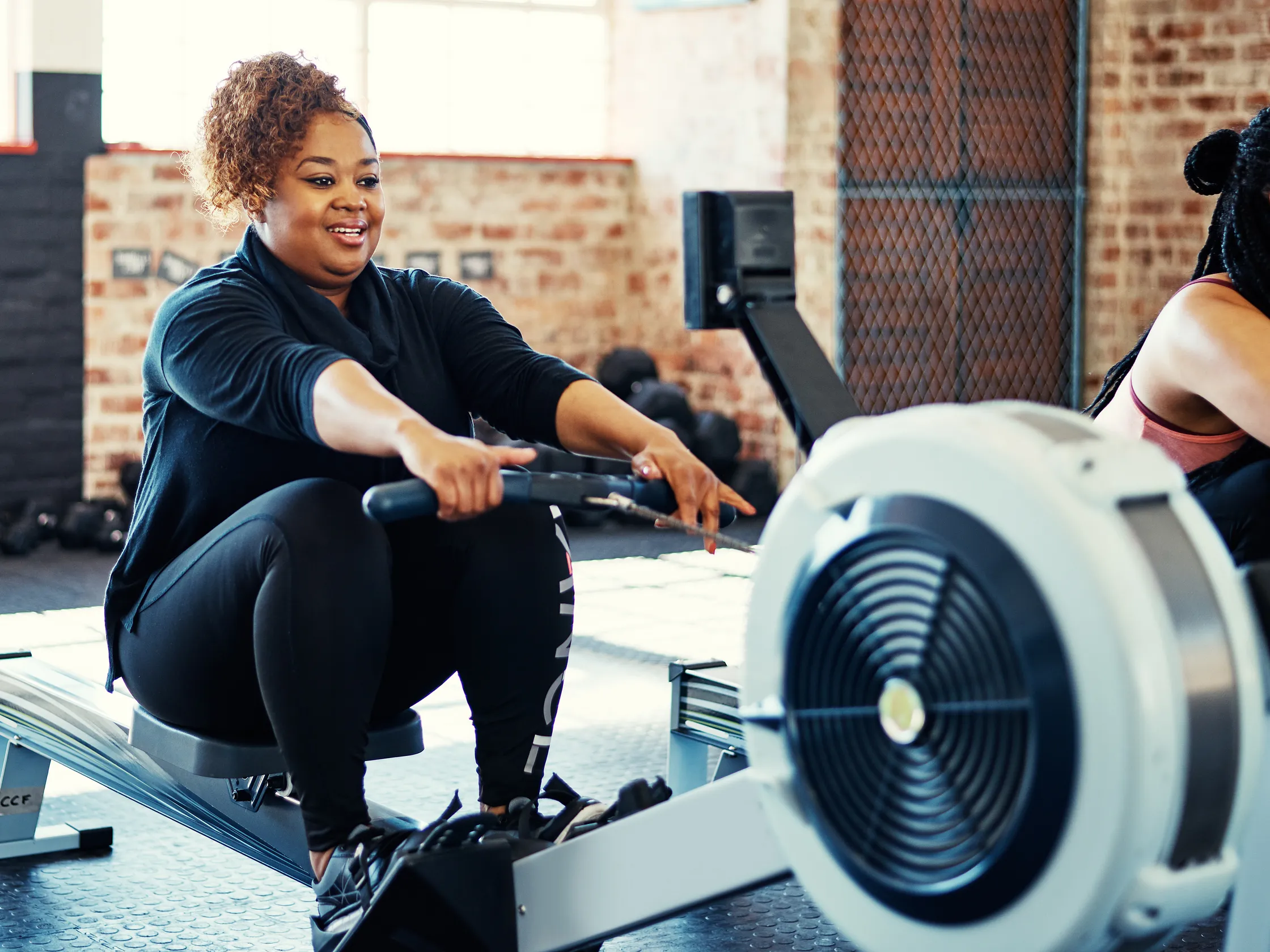 Smiling female athlete practicing proper catch mechanics during a group indoor rowing class at a fitness gym.
