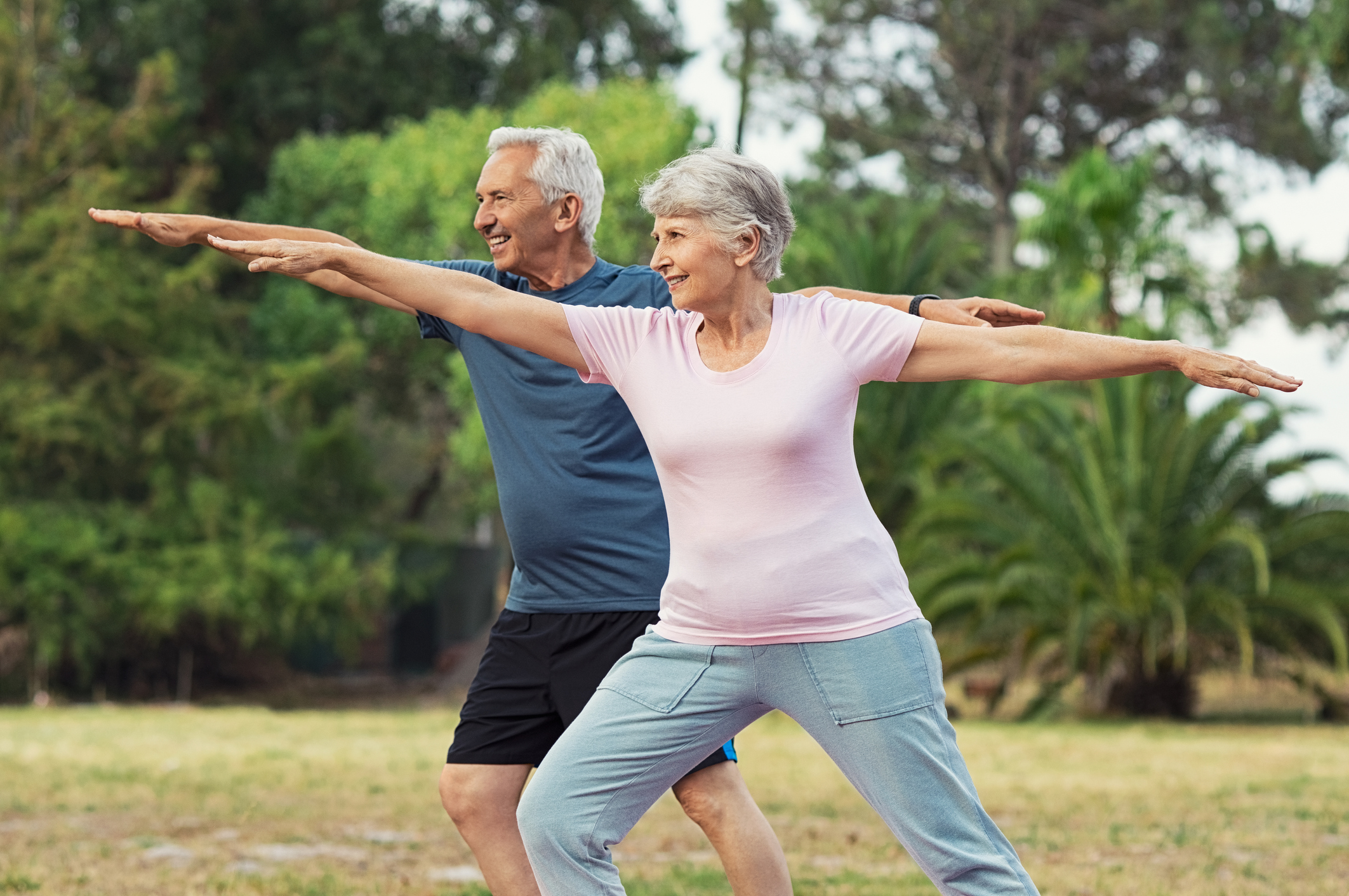 An active senior couple practicing outdoor mobility exercises and lunges to build core strength and flexibility for masters athletic training.