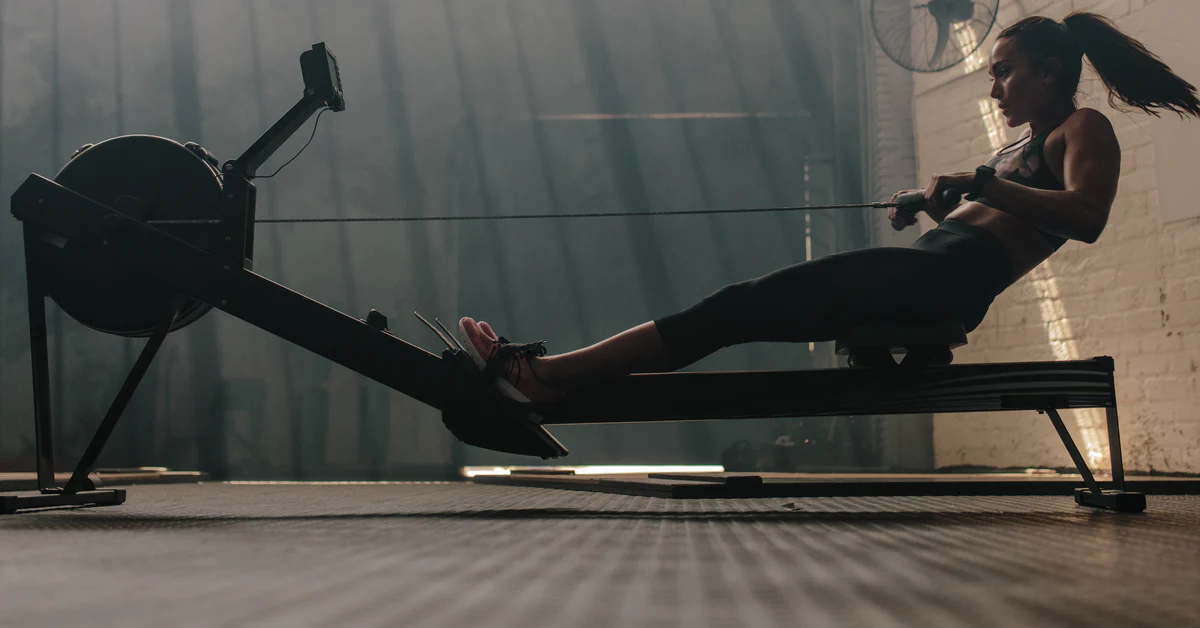A woman pulling the handle of an indoor rower. A woman pulling the handle of an indoor rower.