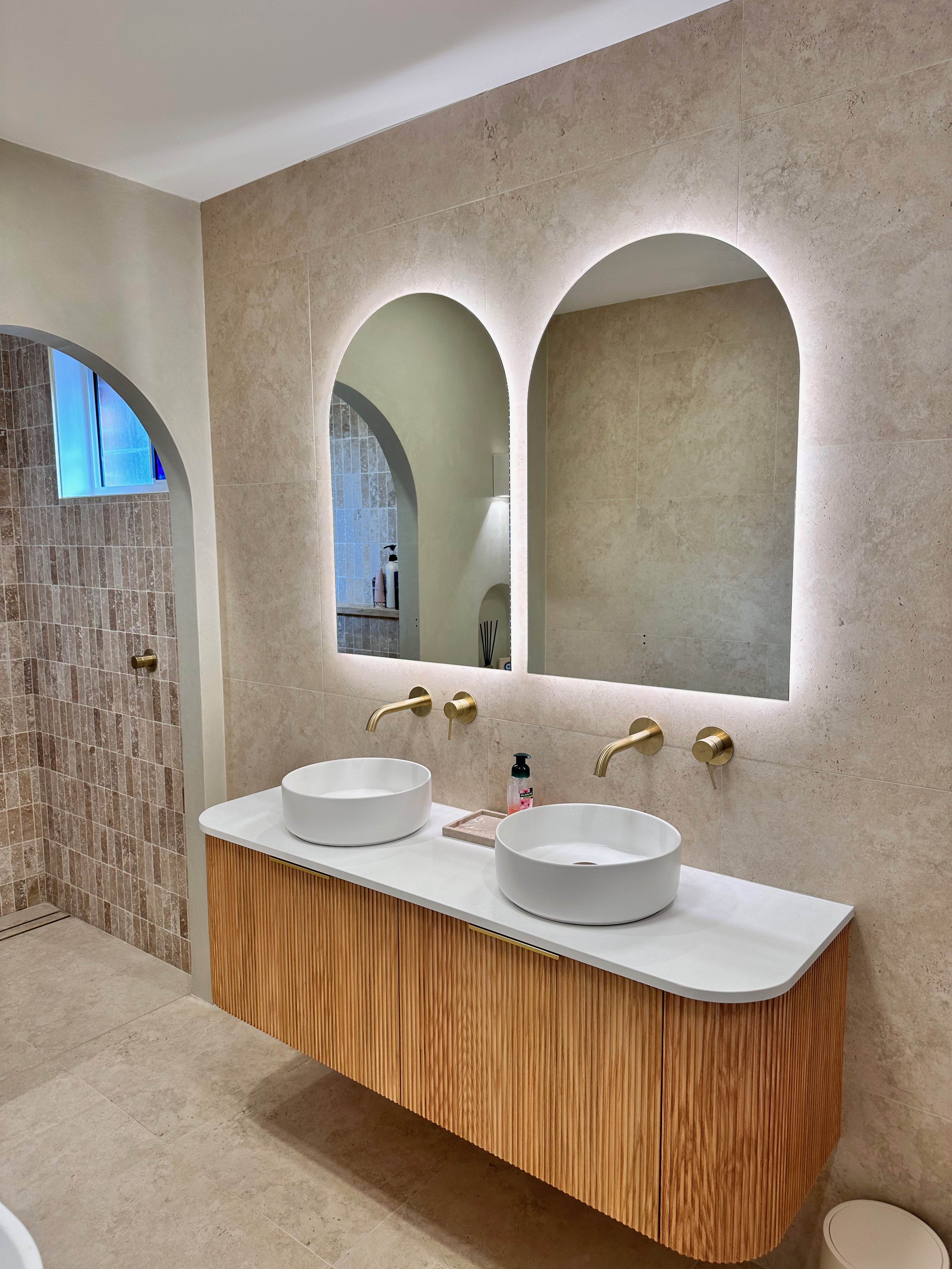 Double arched LED mirrors above a curved timber vanity