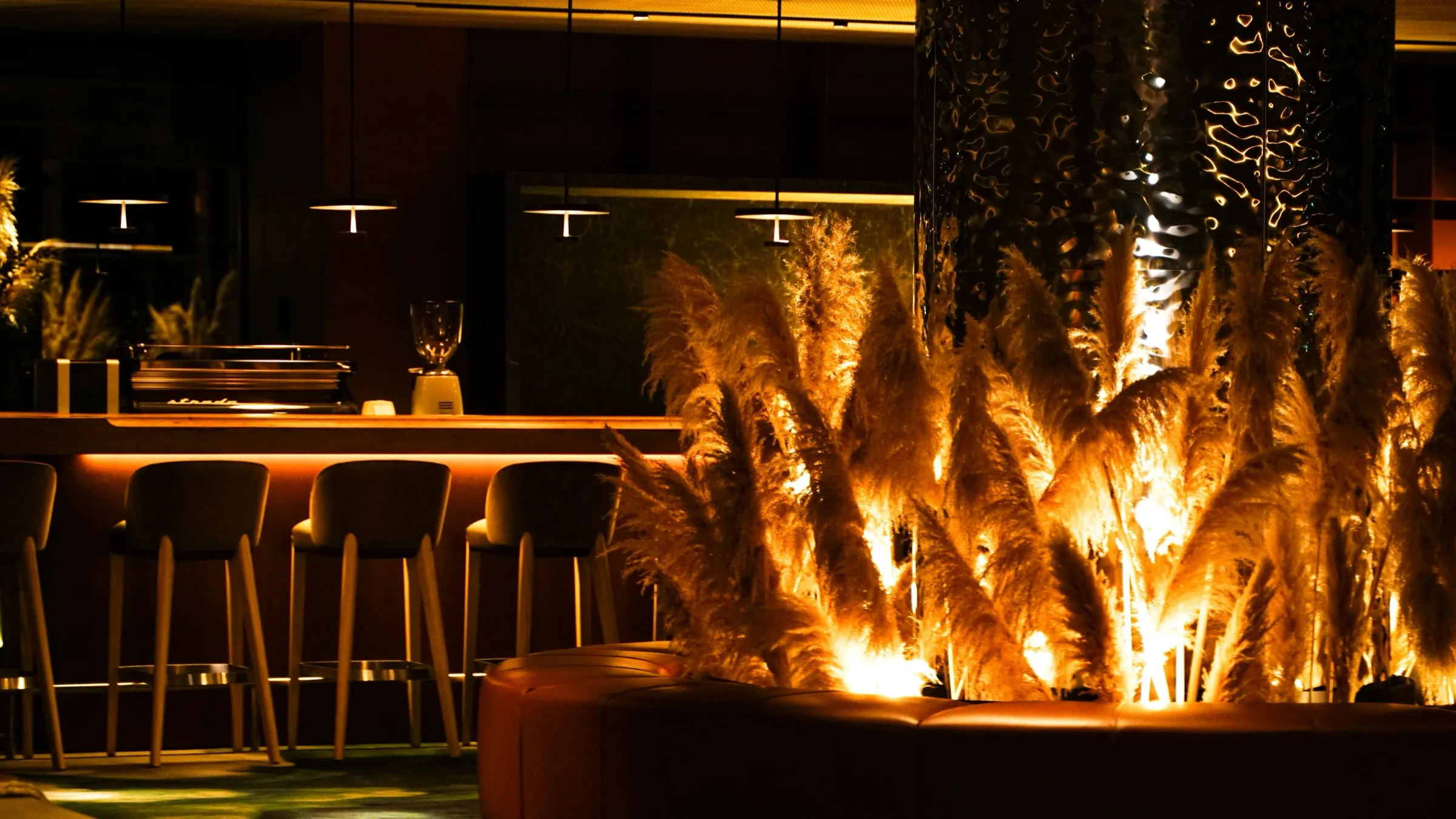 Barra de un hotel boutique con luz ámbar y plumeros iluminados