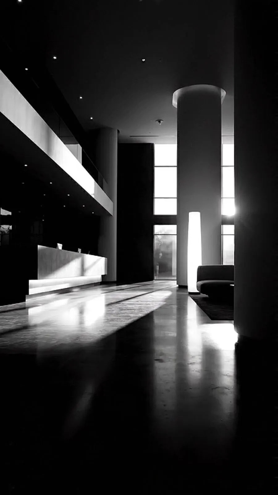Vestíbulo de hotel vacío en blanco y negro, con luz entrando por las ventanas