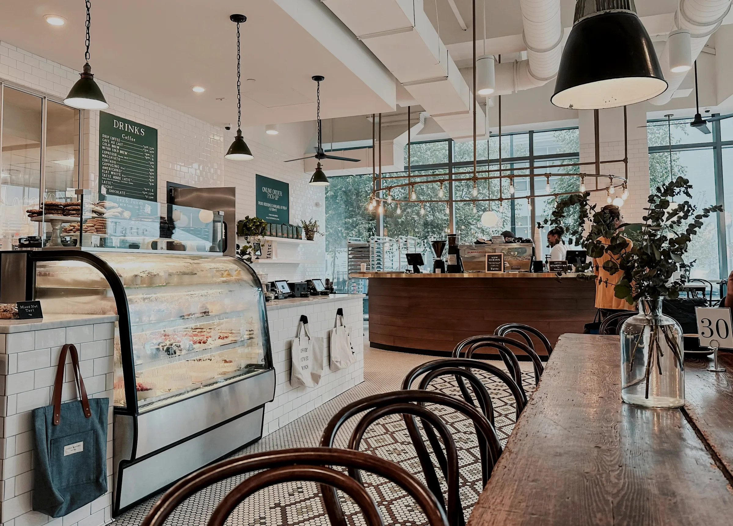 Restaurante con lámparas industriales negras, azulejo blanco y sillas de madera curvada