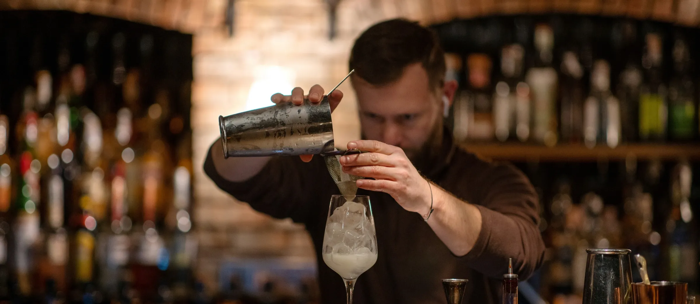 Bartender preparando un cóctel frente a la botellería