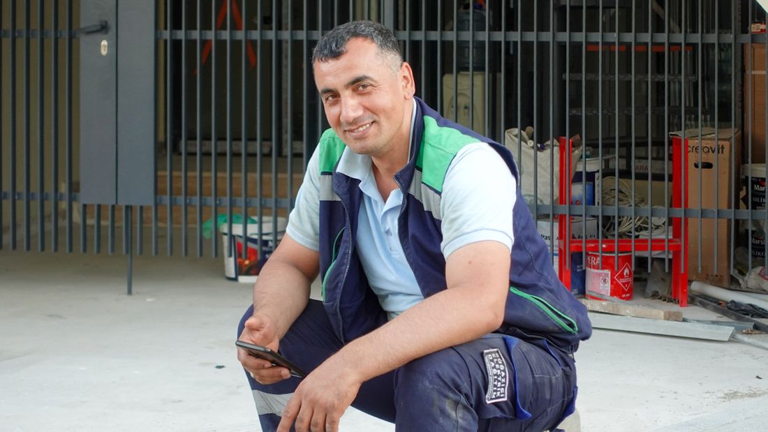 Smiling contractor checking his phone outside a job site. Illustrative stock photo.