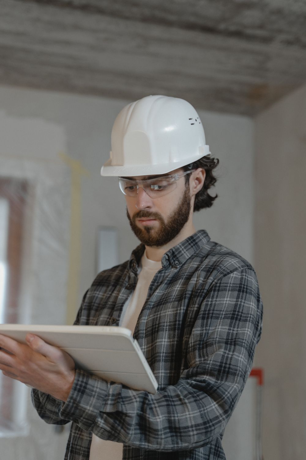Contractor in a hard hat reviewing job details on a tablet inside a home renovation. Illustrative stock photo.