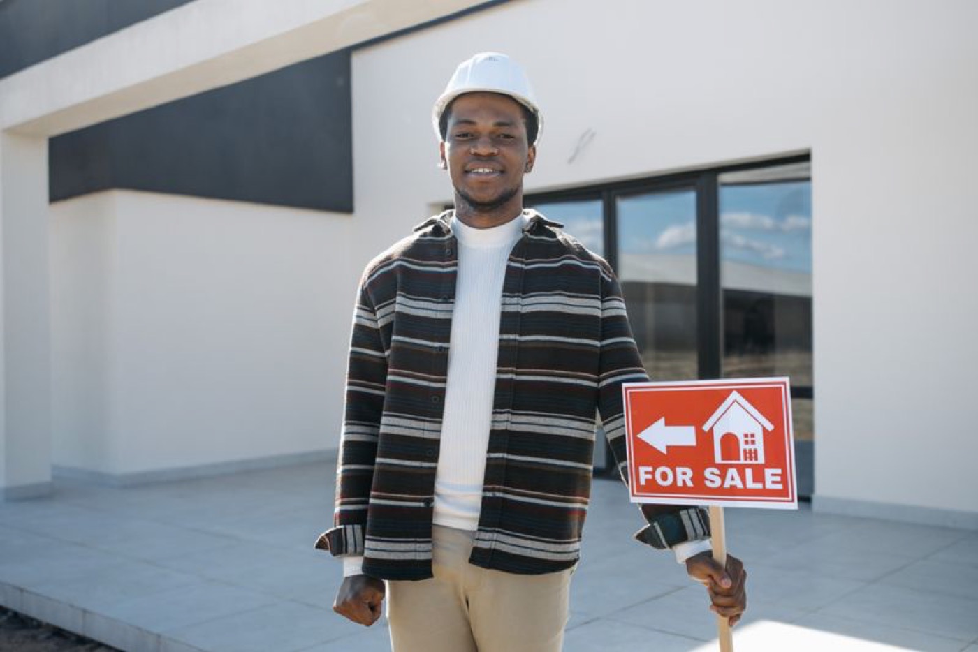 A real estate agent holding a For Sale sign in front of a modern home — illustrative stock photo