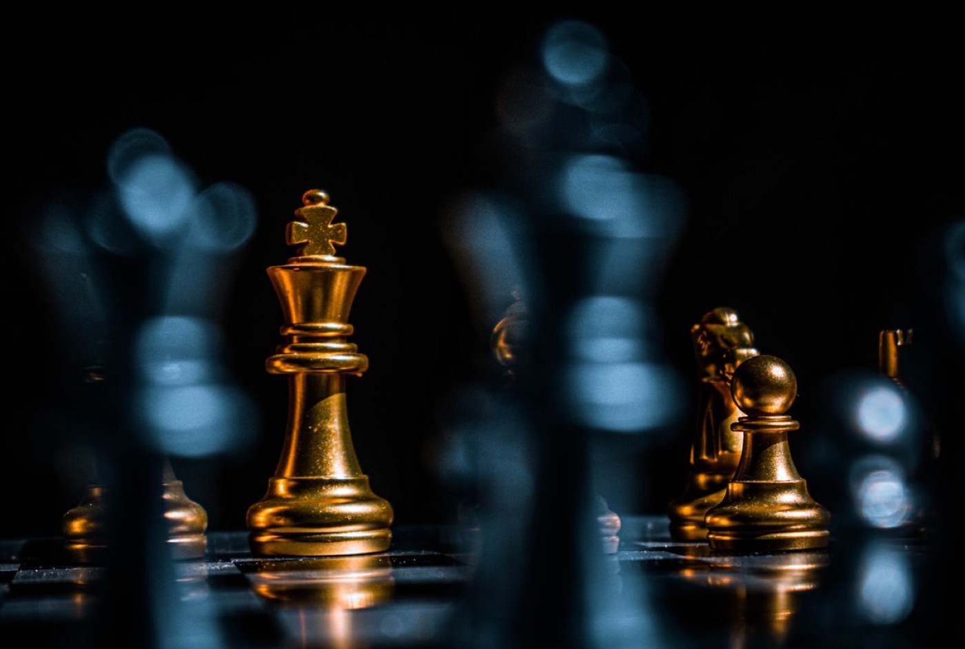 A gold chess king standing lit against a dark board — illustrative stock photo