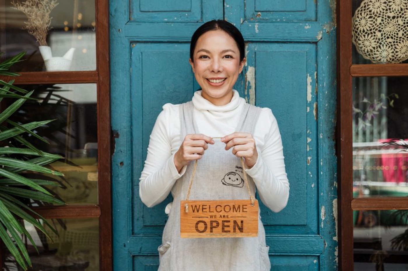 A shop owner holding a Welcome, We're Open sign at her door — illustrative stock photo
