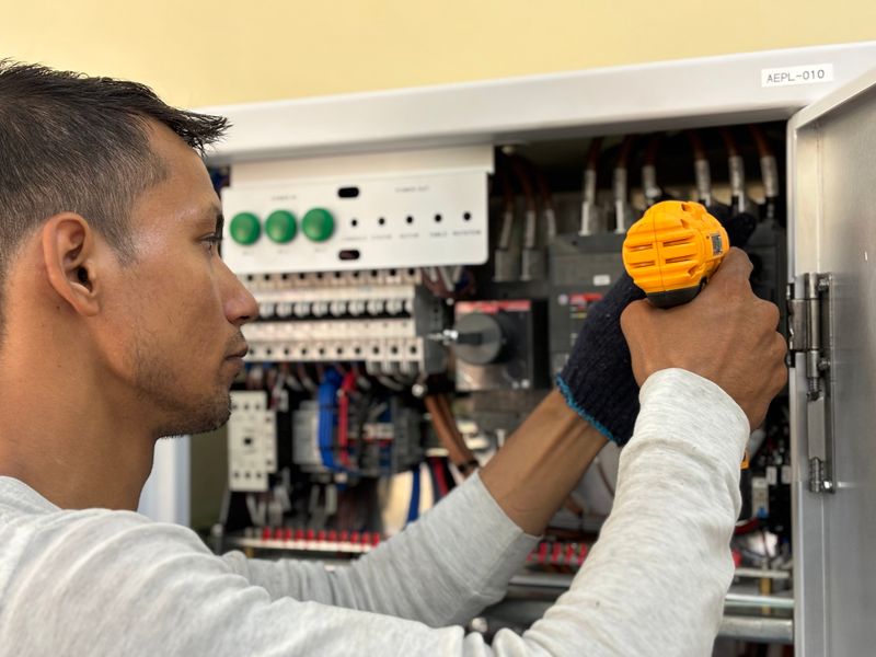 Electrician working on a breaker panel with a drill. Illustrative stock photo.