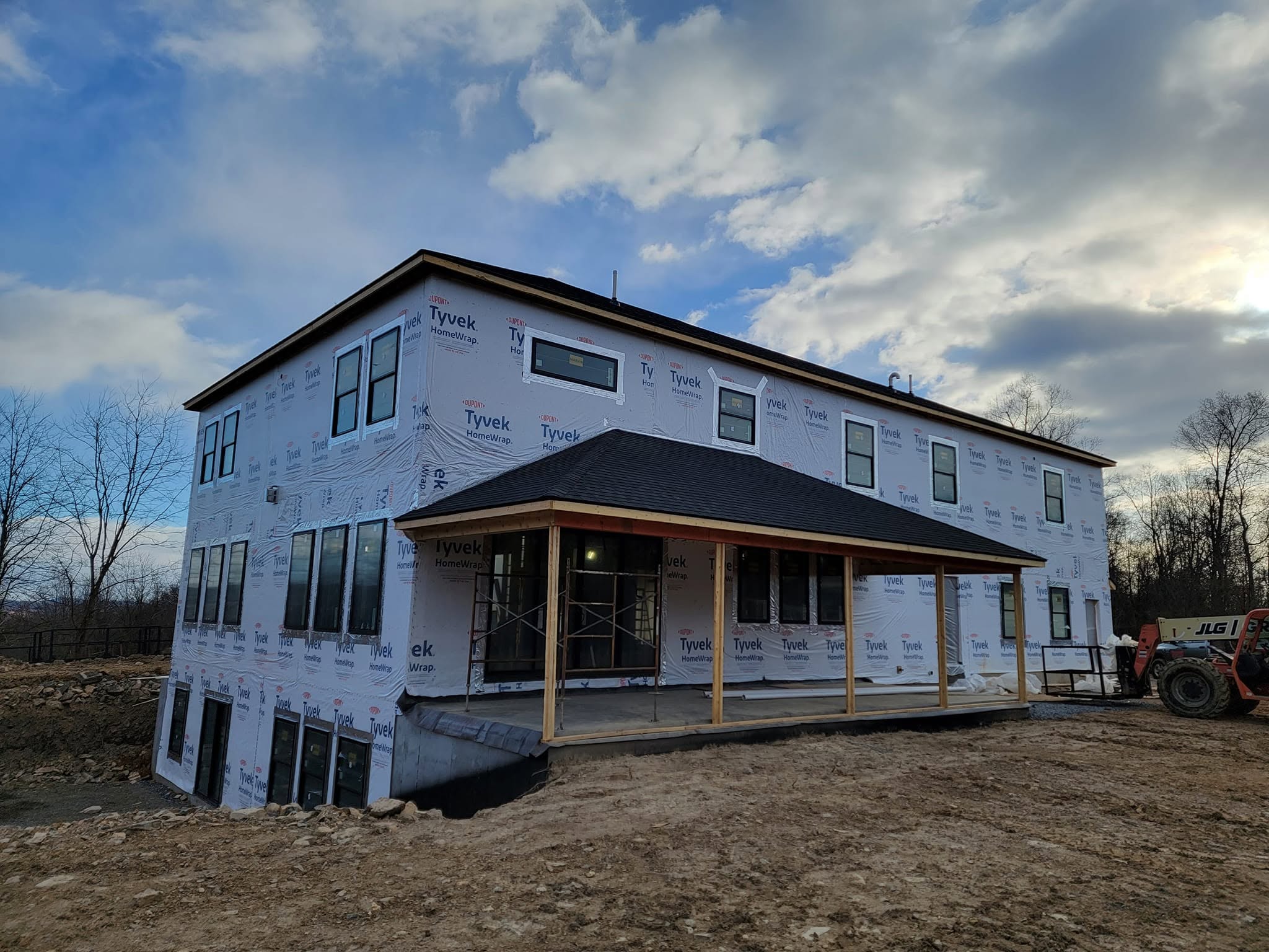 Two story custom home under construction with house wrap and a timber framed porch