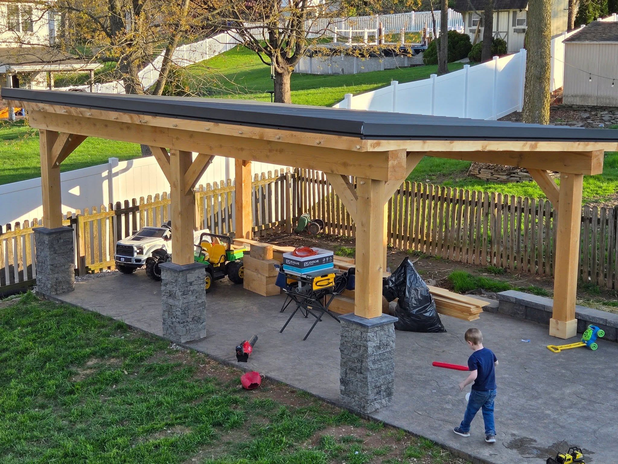 Finished timber pavilion with stone columns and a wood ceiling in a fenced back yard