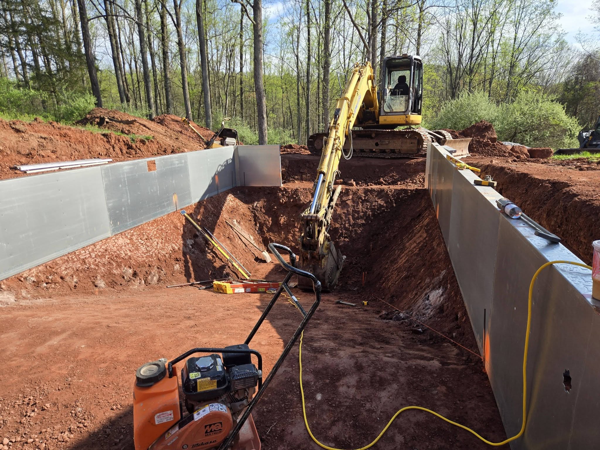 Excavator working between steel pool walls in red clay on a Harcon Services job site