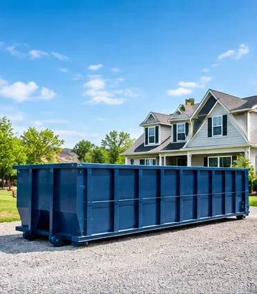 Roll-off dumpster on a gravel pad in front of a two-story home