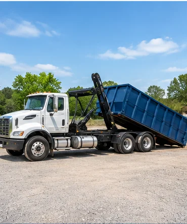 Roll-off truck unloading a blue dumpster onto a gravel lot