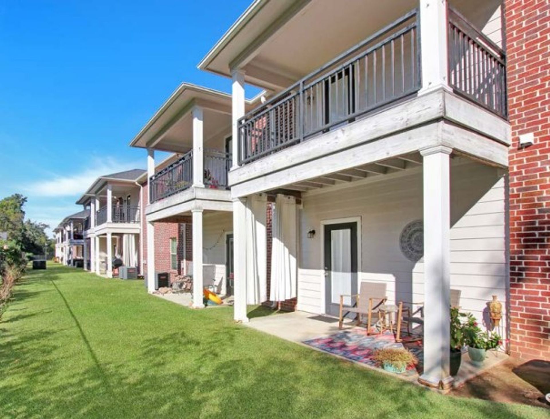Ground-floor covered patio with brick columns, a balcony above and lawn