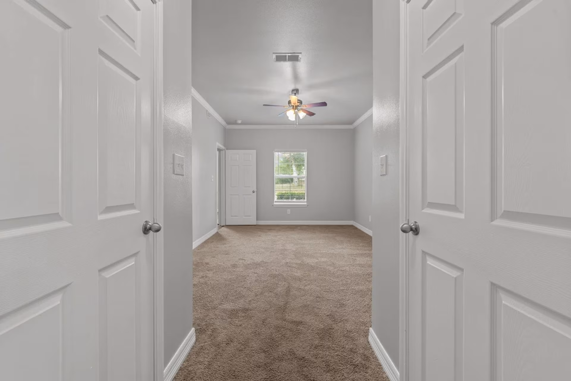 Carpeted bedroom seen through double doors, with a window and ceiling fan