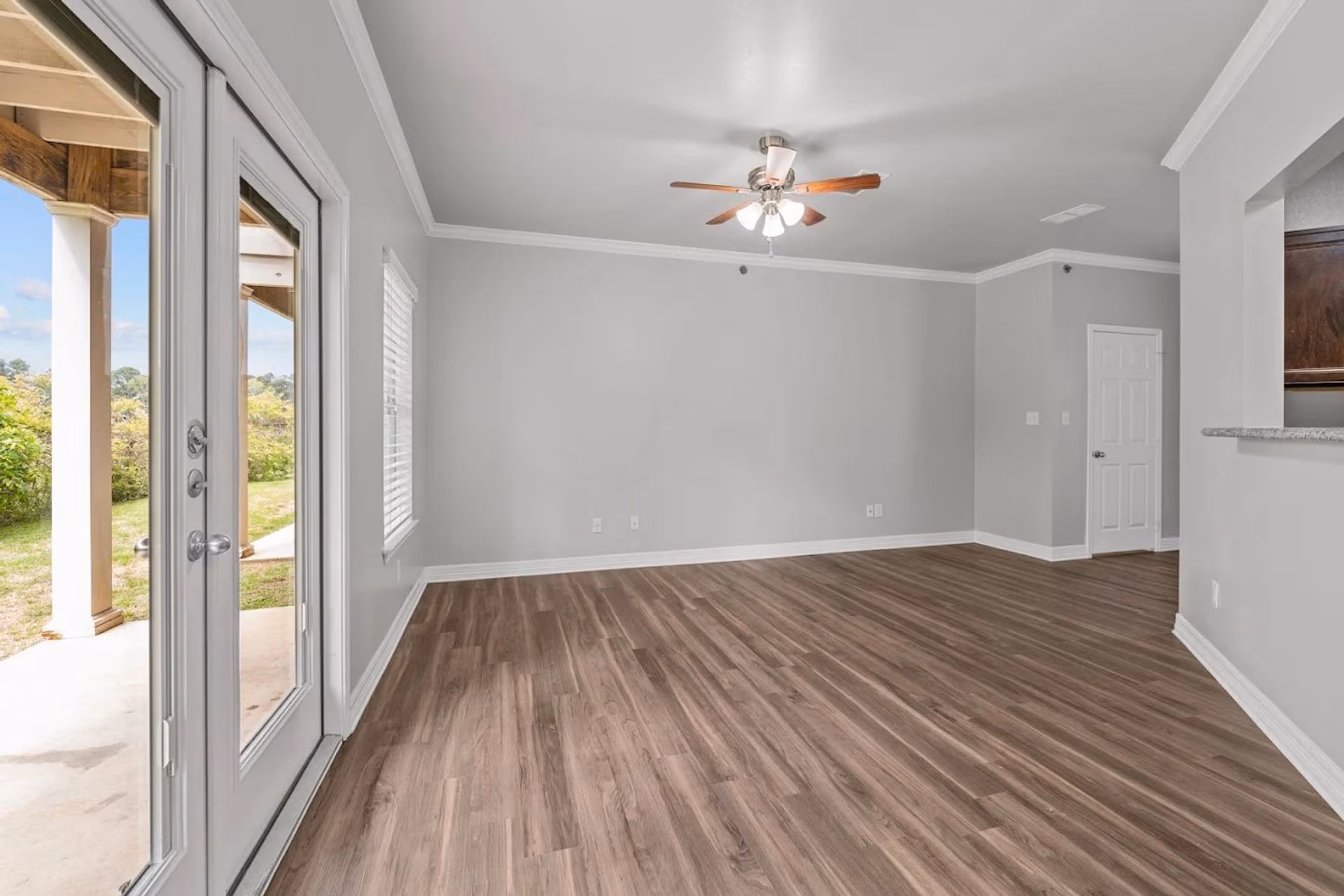 Living area with wood-look plank flooring, ceiling fan and French doors to a patio