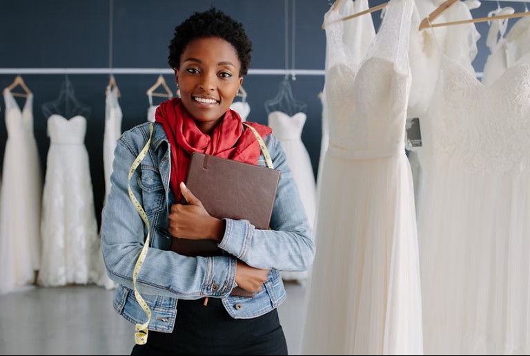 happy black wedding planner in front of wedding dresses