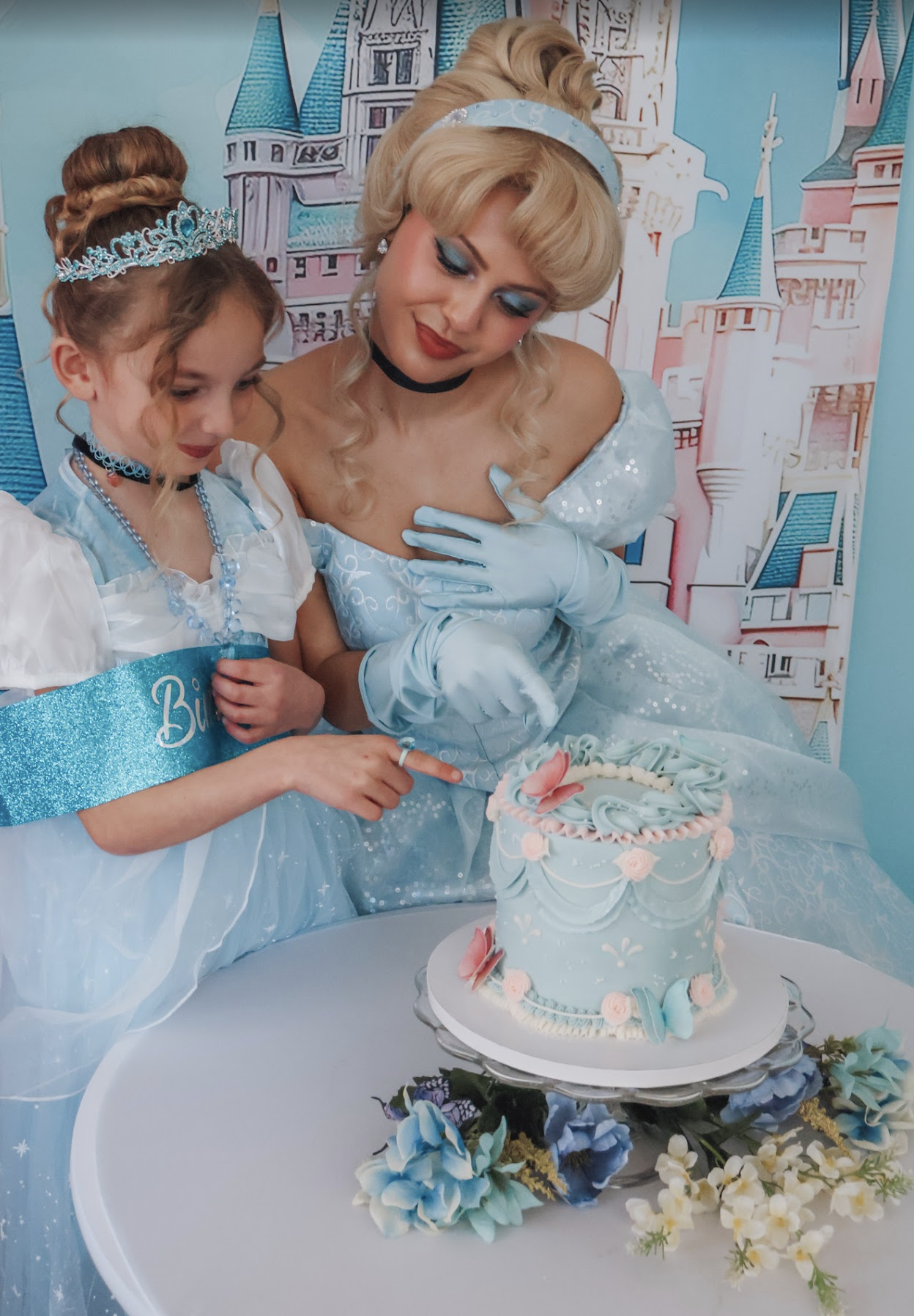 Cinderella and a birthday child beside a pale blue cake at a princess celebration