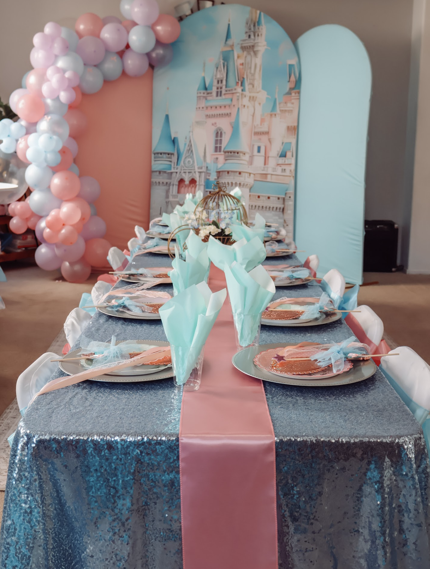Princess party table with shimmering blue linens, pink runner, white chairs and a pastel castle backdrop