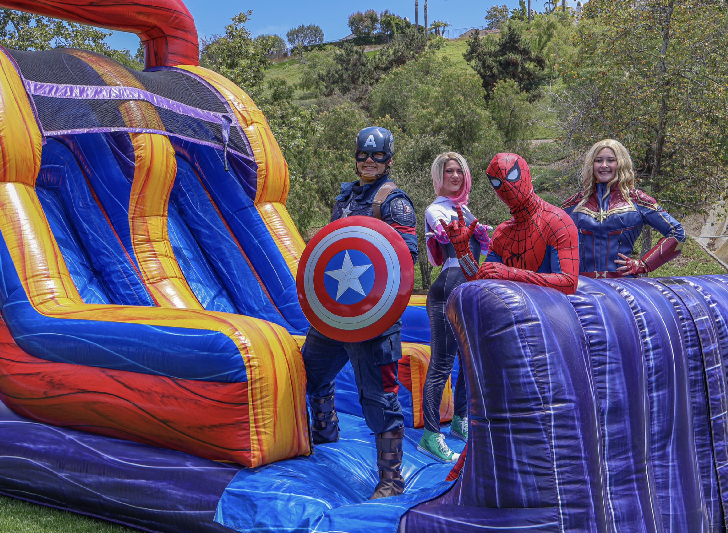 Captain America, Spider-Gwen, Spider-Man and Captain Marvel posing beside a colorful inflatable slide