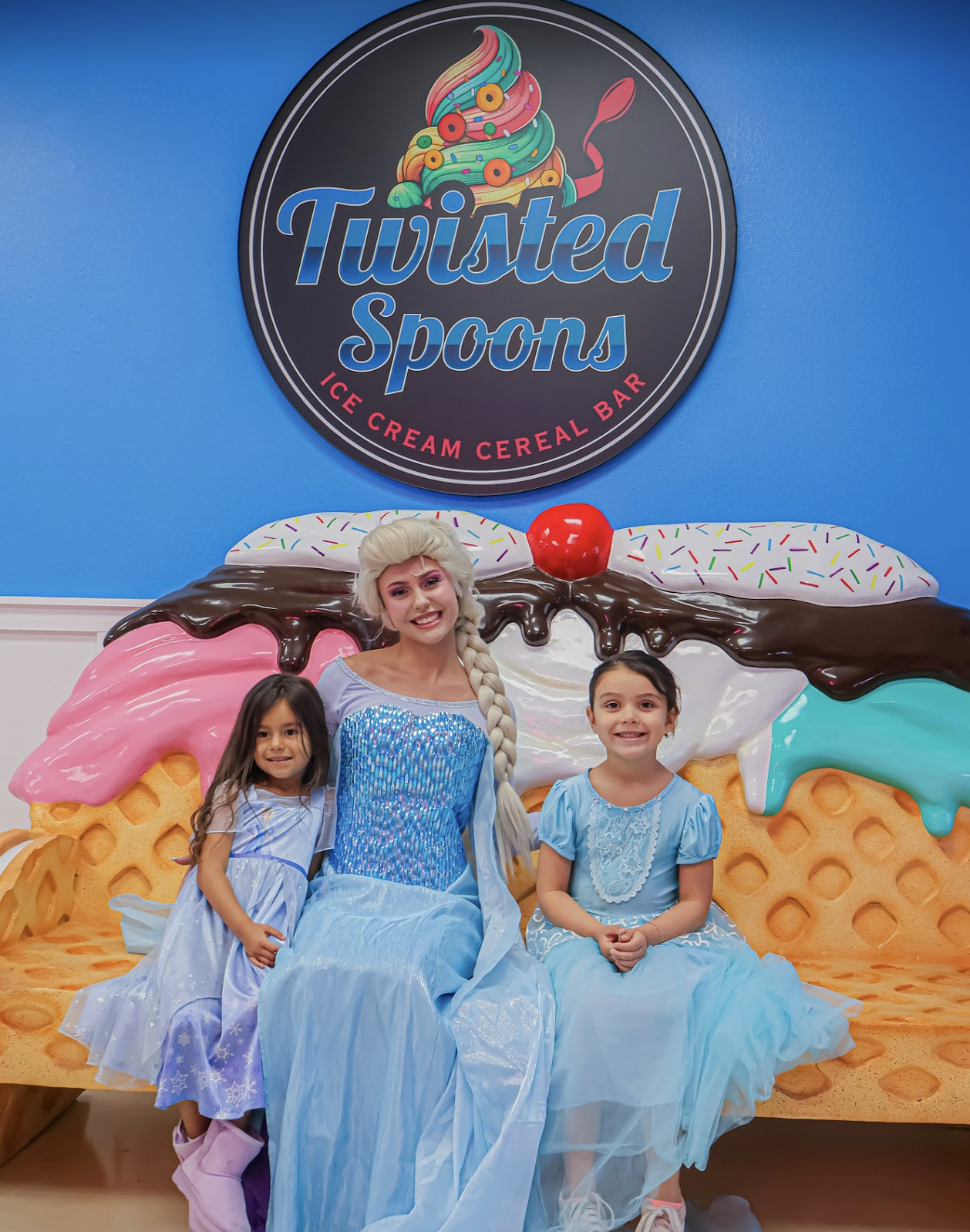 Elsa posing with two young guests beneath the Twisted Spoons ice cream cereal bar sign