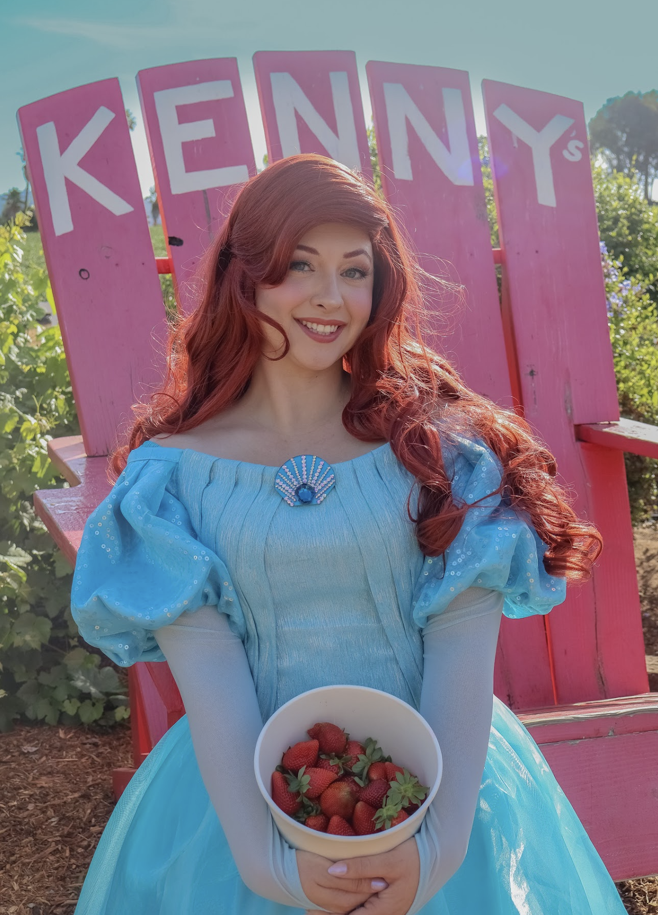 Ariel seated in a pink Kenny's chair with a bowl of strawberries
