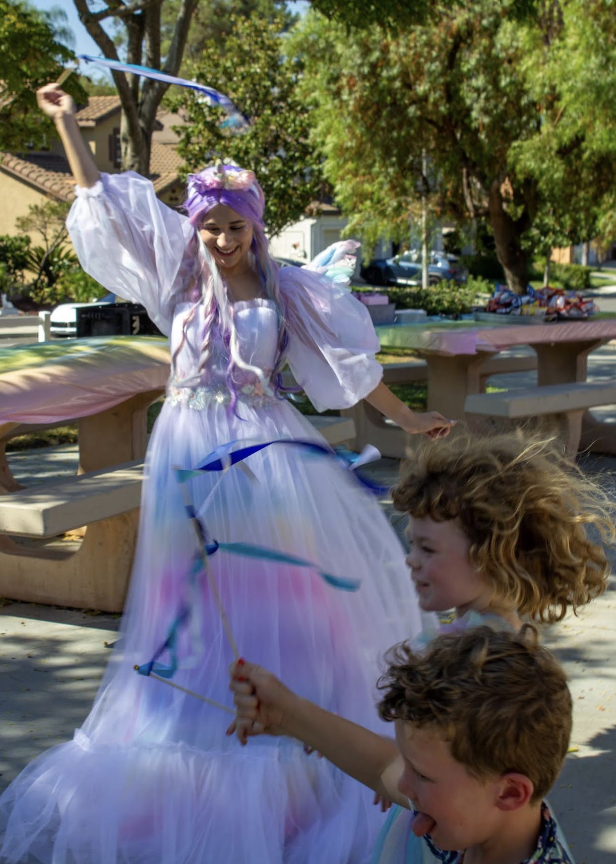 A unicorn-themed performer and young children playing with ribbon wands outdoors