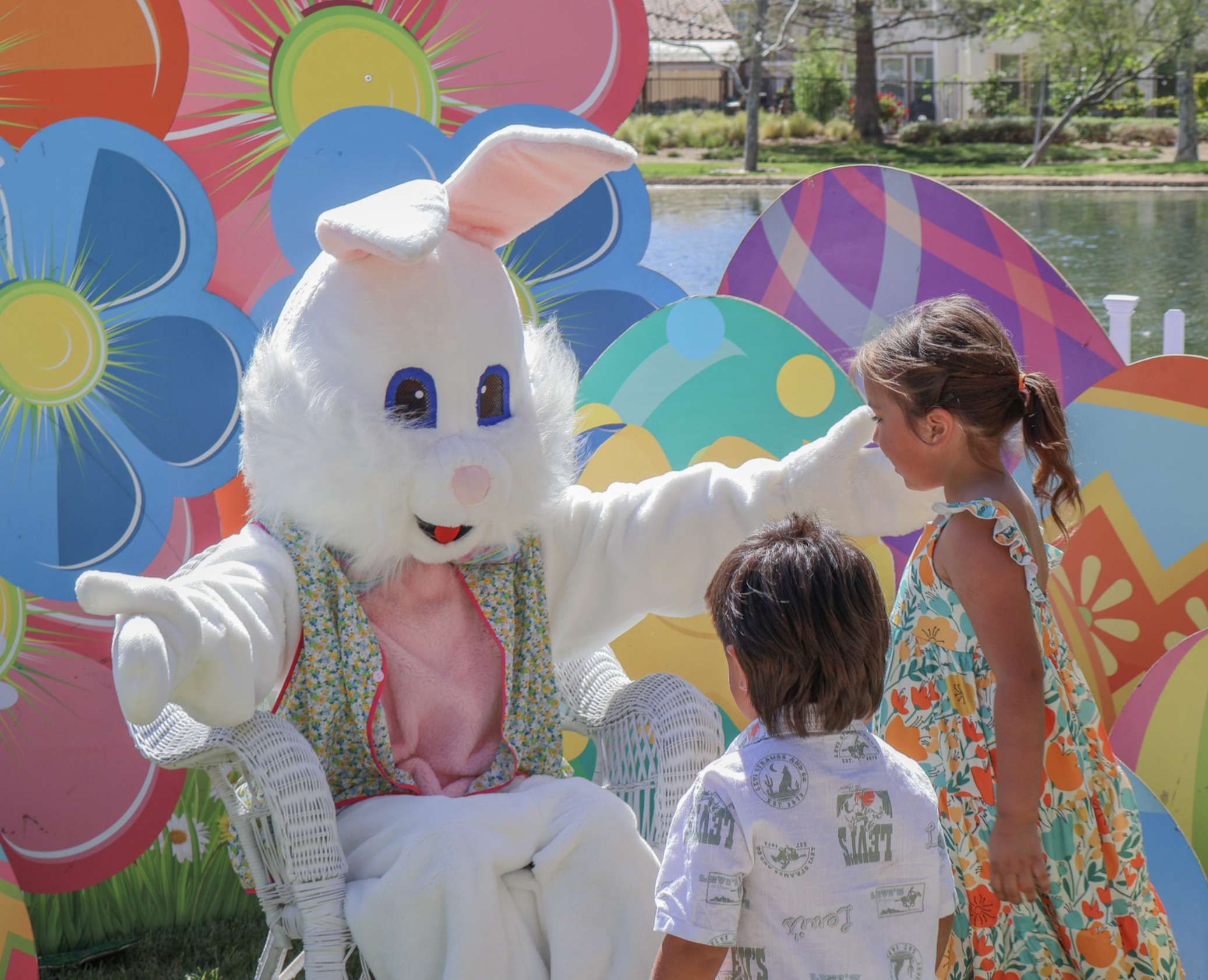 The Easter Bunny greeting two children in front of a bright spring photo backdrop