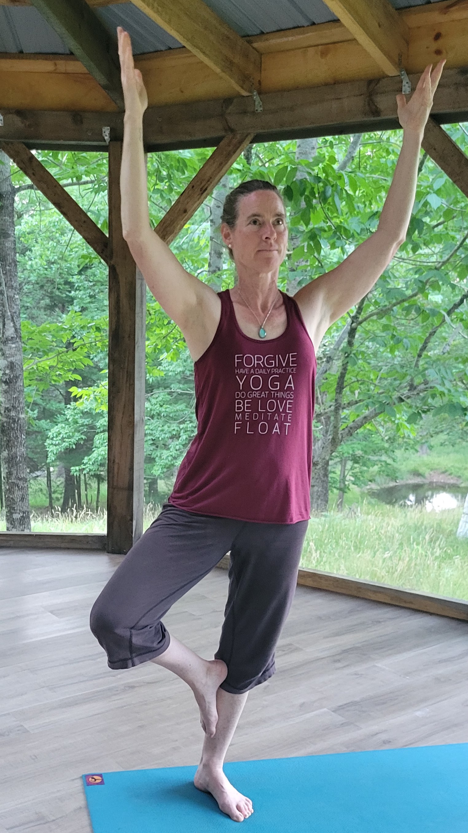 Balance to Bliss Owner Tracy Murdoch performs Tree pose in a gazebo. There are green trees in the background.