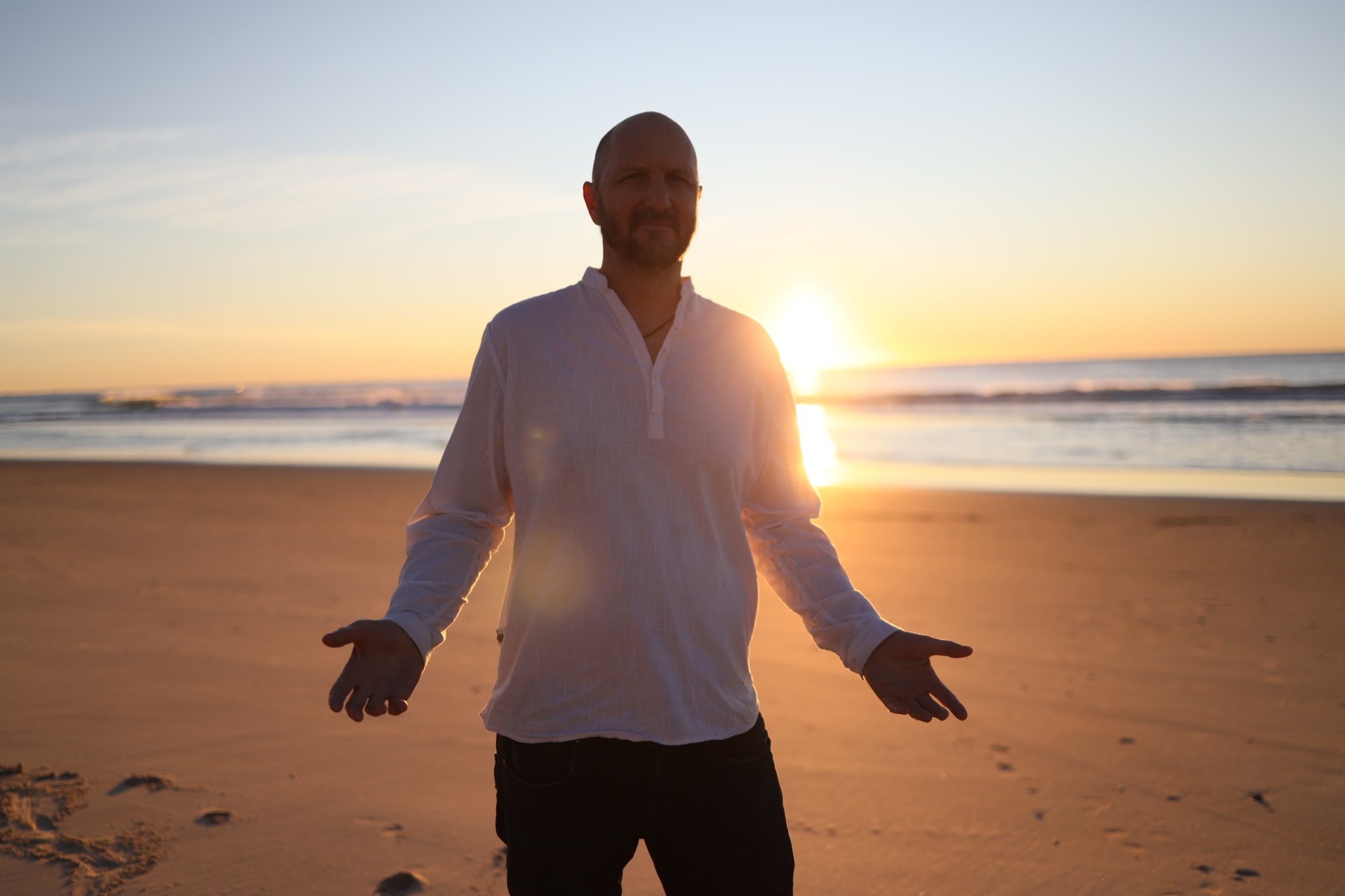 Chris on the beach at sunrise, arms open