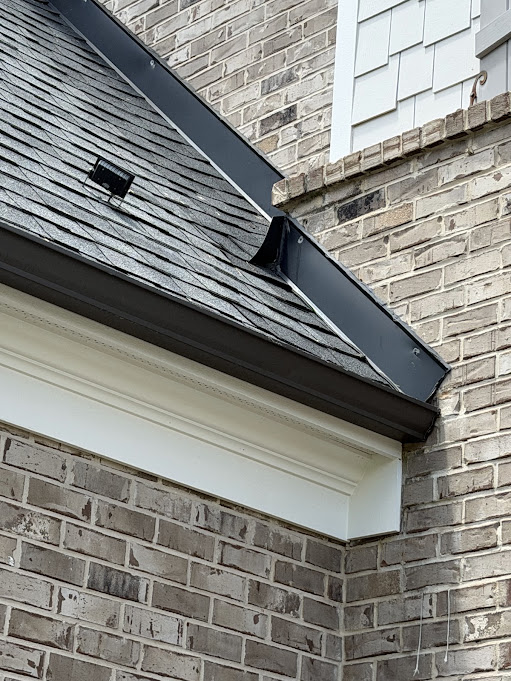 Dark counter flashing set into a painted brick wall above a shingle roof section