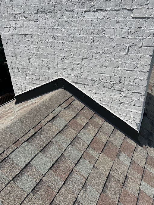 New dark counter flashing installed along a painted brick wall above the shingle line