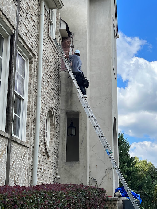 Technician on a ladder against a stucco wall inspecting the roof to wall junction