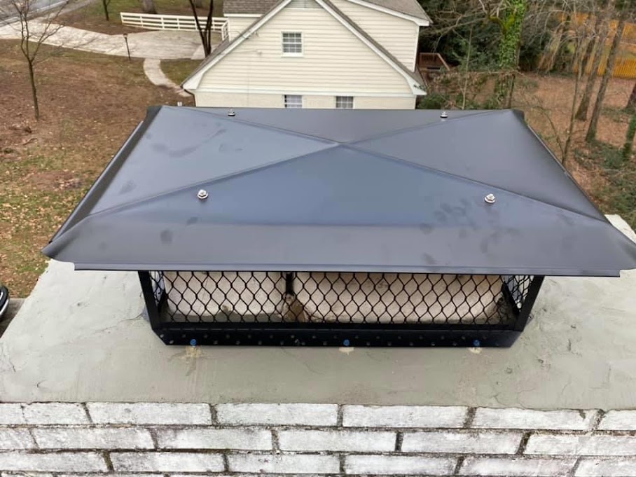 New black chimney cap with mesh screening installed on a white masonry crown