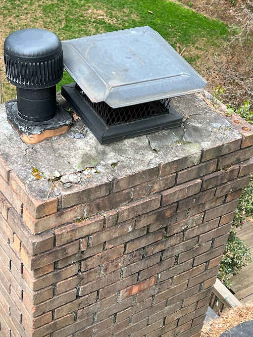 Black flue cap beside a galvanized chase cover on a brick chimney top